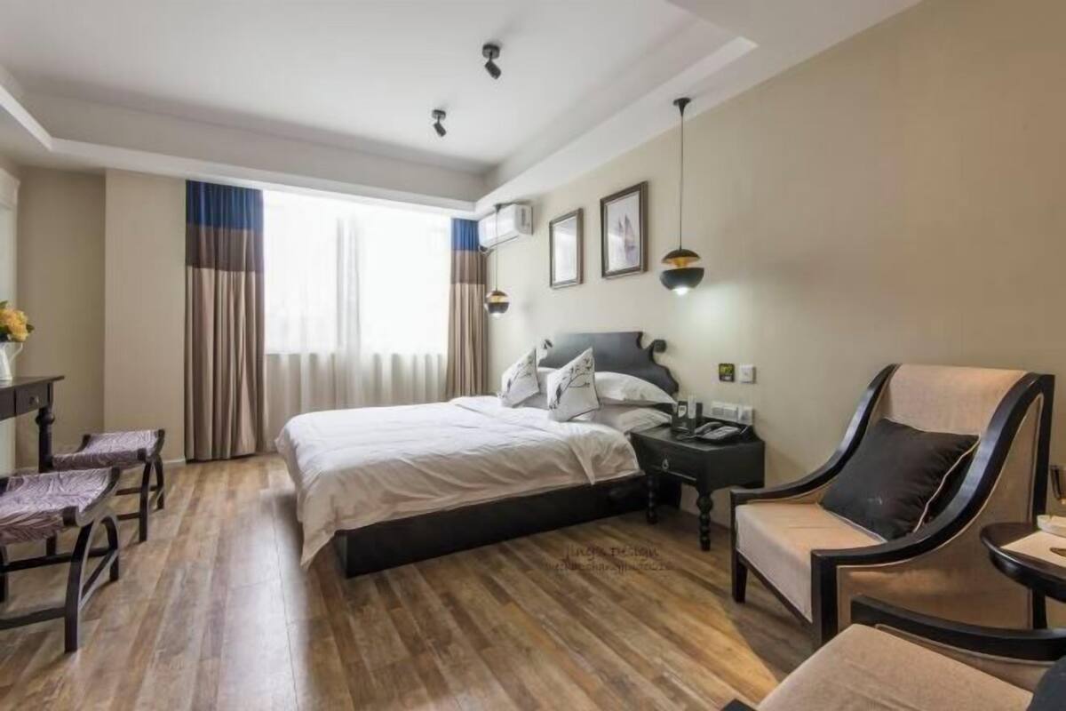 Habitación de hotel con cama, escritorio, silla, mesita de noche y ventana con cortinas.