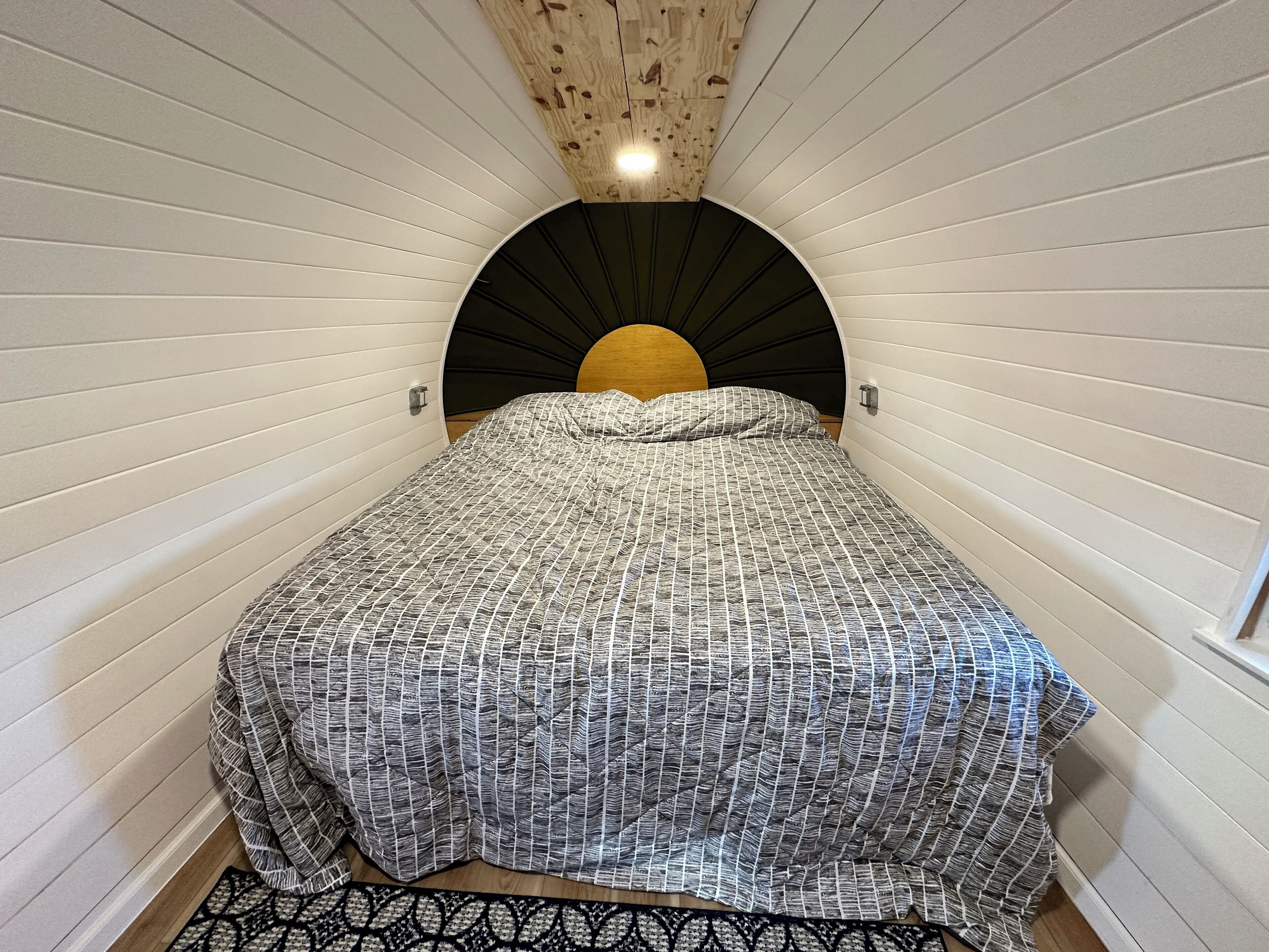 Et soveværelse med buet loft, en seng med et mønstret sengetæppe og en træsenggavl.