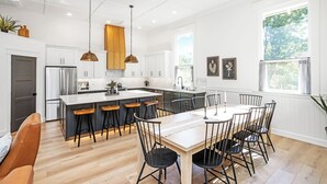 Una cocina moderna con una isla central, taburetes de bar de madera y una mesa de comedor con sillas.