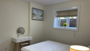Ein Schlafzimmer mit einem Bett, einem Nachttisch mit Spiegel, einem Fenster mit Jalousien und einem Bild an der Wand.
