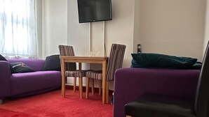 A living room with a red carpet, purple sofas, a wooden table, striped chairs, and a TV mounted on the wall. - Curzon St - 4 Beds, Sleeps 7 with Street Parking (Reading)