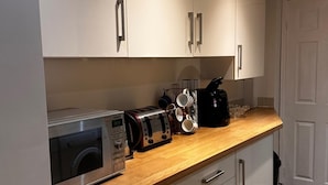 A kitchen with a microwave, toaster, coffee maker, and a cup holder with mugs. - Curzon St - 4 Beds, Sleeps 7 with Street Parking (Reading)