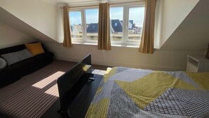 Une chambre avec un plafond en pente, un lit, un bureau et une fenêtre avec des rideaux.