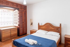 A bedroom with a wooden bed, a blue bedspread, and a window with metal bars.