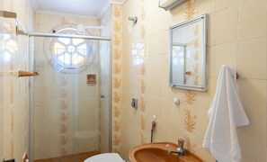 A bathroom with a glass shower enclosure, a sink with a mirror, and a towel hanging on the wall.