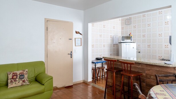 Un espacio habitable compacto con un sofá verde, una pequeña cocina con microondas y refrigerador, y una mesa de comedor de madera.