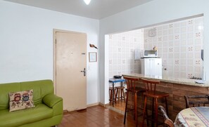 A compact living space with a green sofa, a small kitchen area with a microwave and refrigerator, and a wooden dining table.