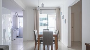 A modern dining area with a glass partition, a chandelier, and a view of the outside. - 2-bed Apt w/ BBQ - Downtown Bombinhas Caa103 (Bombinhas)