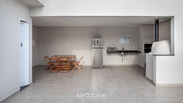 Eine moderne Küche mit Kühlschrank, Mikrowelle, Spüle und einem Pizzaofen. Es gibt einen Holztisch mit Stühlen.