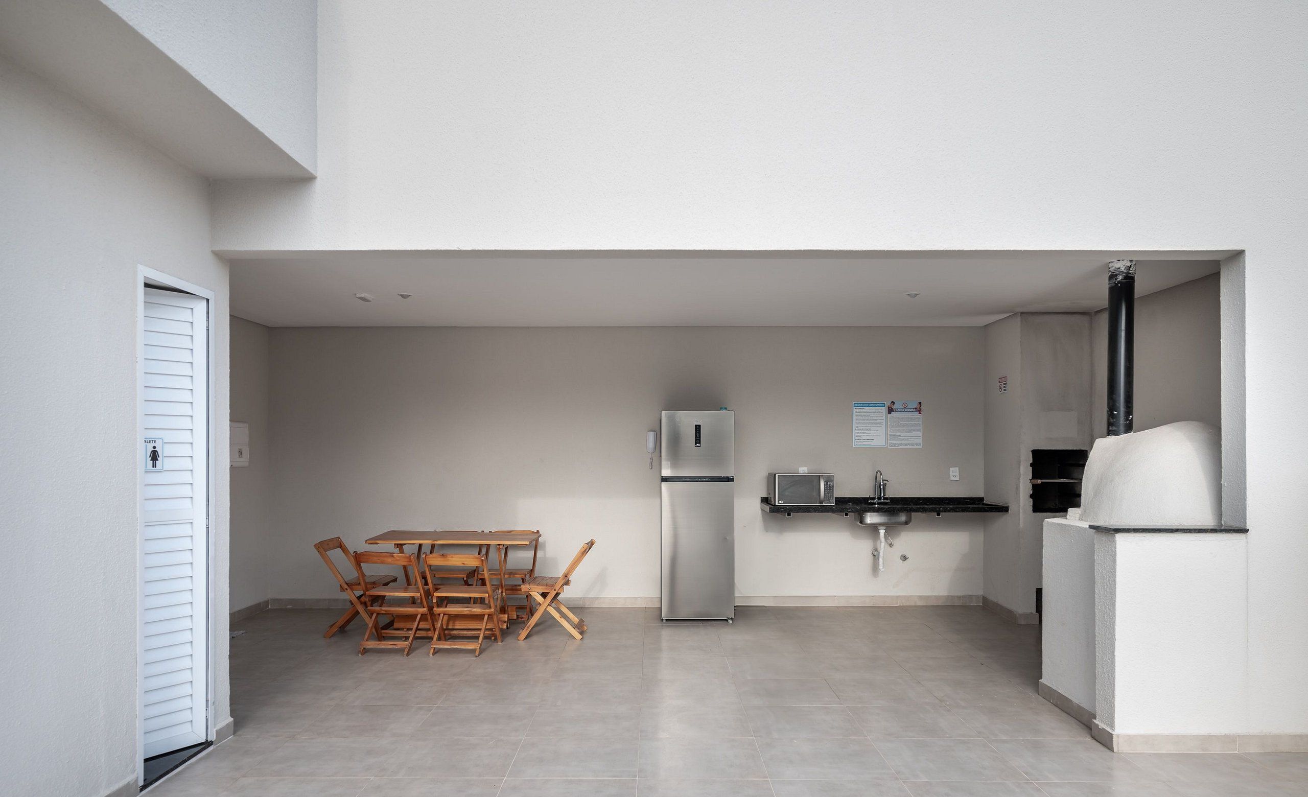 A modern kitchen with a refrigerator, microwave, sink, and a pizza oven. There is a wooden dining table with chairs.