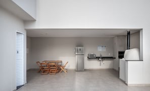 A modern kitchen with a refrigerator, microwave, sink, and a pizza oven. There is a wooden dining table with chairs. - Apt With Barbecue 2 min From Tenorio Beach Cah014 (Ubatuba)