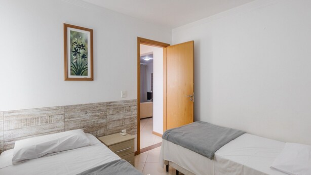 A bedroom with two beds, a wooden door, a framed picture on the wall, and a tiled headboard.