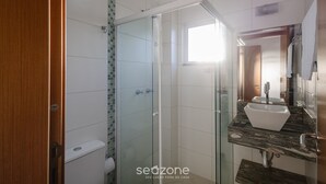 A bathroom with a glass-enclosed shower, a white sink, and a wooden door.