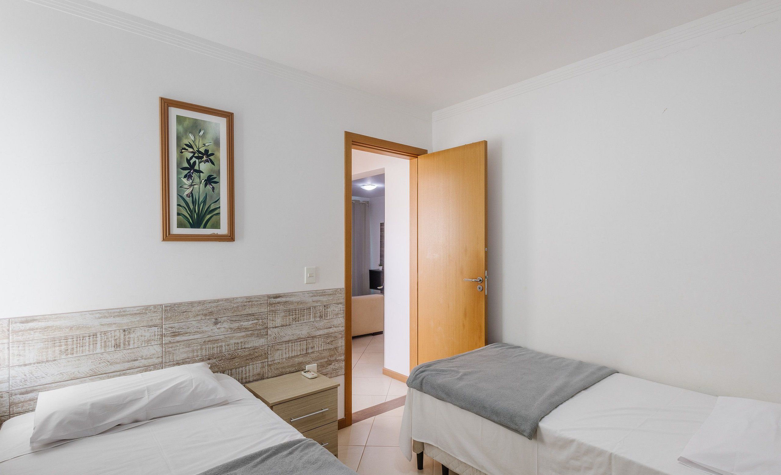 Ein Schlafzimmer mit zwei Betten, einer Holztür, einem gerahmten Bild an der Wand und einem Fliesen-Kopfteil.