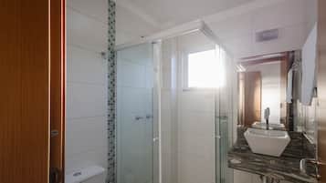 Un baño con ducha envuelta en vidrio, un lavamanos blanco y una puerta de madera.