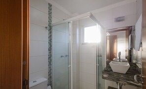 Un baño con ducha envuelta en vidrio, un lavamanos blanco y una puerta de madera.