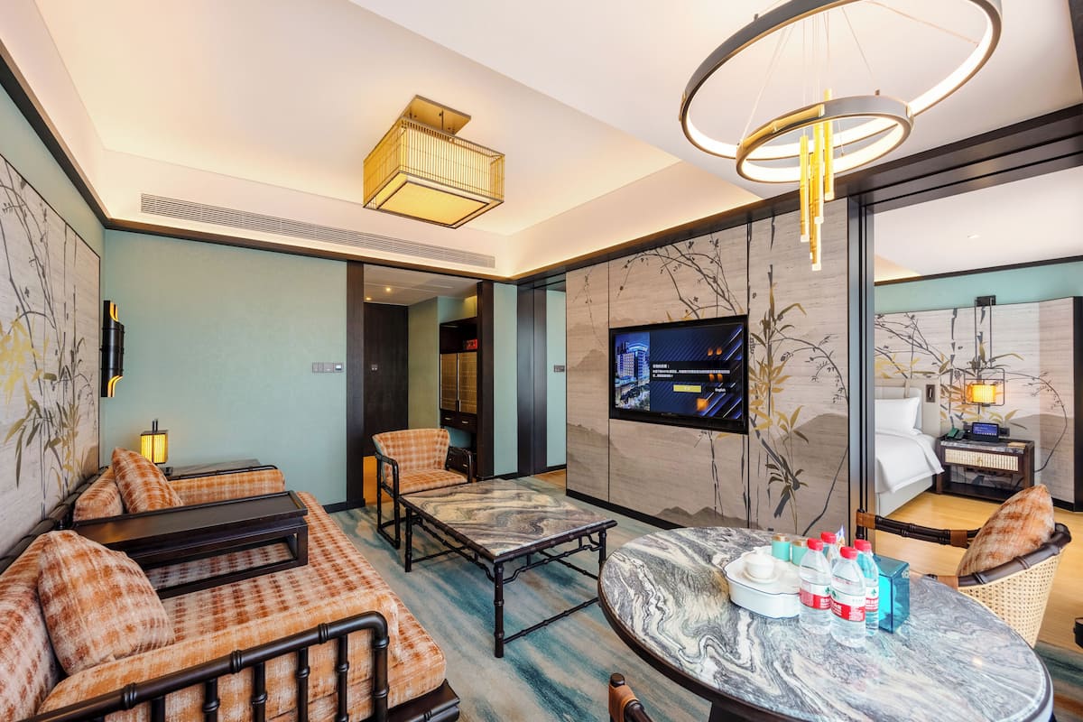 A modern hotel room with a sofa, a coffee table, a TV, and a bed.