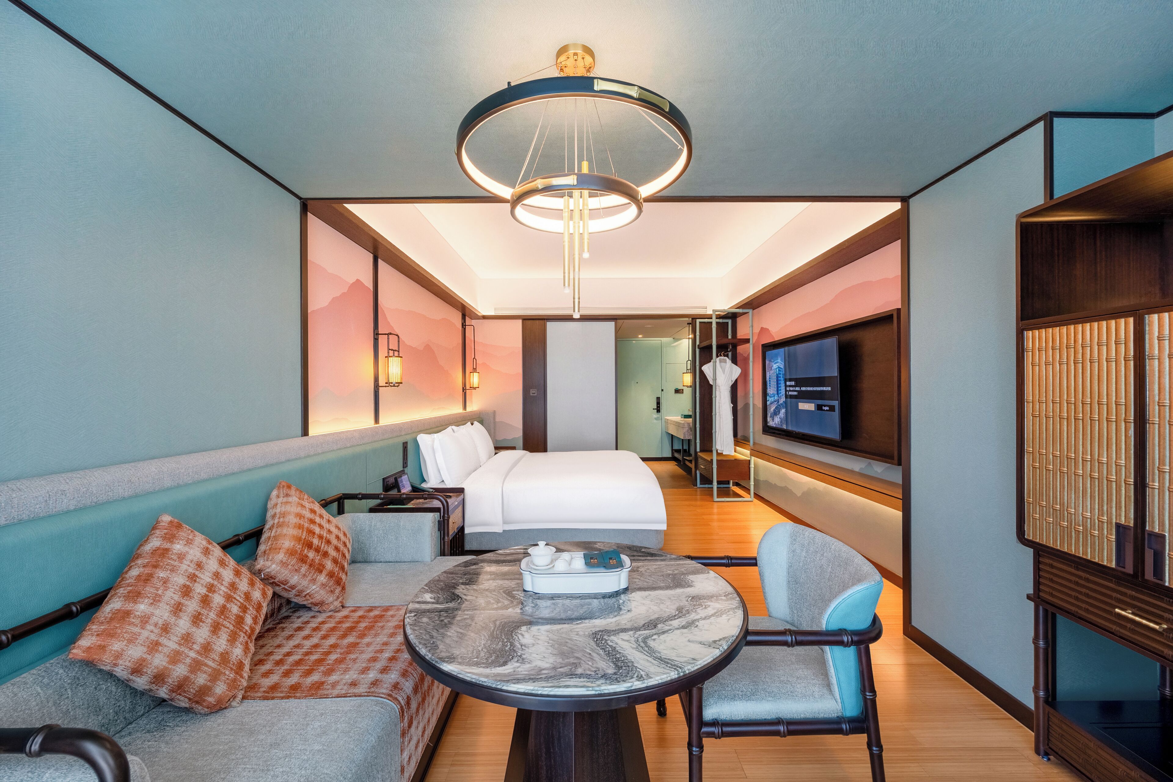 Una habitación de hotel moderna con cama, zona de estar, televisión y un ventanal grande.