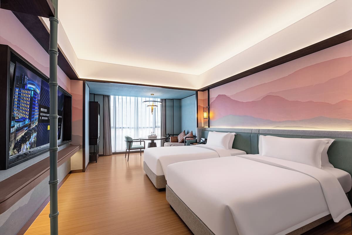 A hotel room with two beds, a TV, a desk, and a view of a cityscape.