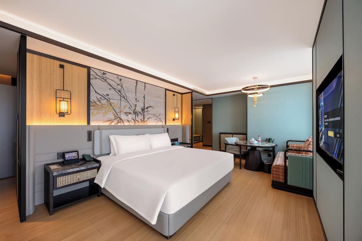 A modern hotel room with a large bed, bedside tables, a desk, and a TV.