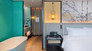 A modern hotel room with a large bed, a bathtub, a vanity with a mirror, and a wall-mounted light fixture. - DIOTEL (Shantou)