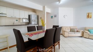 A modern kitchen with white cabinets, a microwave, and a refrigerator. There is a dining table with chairs and a sofa in the living area. - 3BR apt W/bbq 240m sea Bombas/sc Cay0123 (Bombinhas)