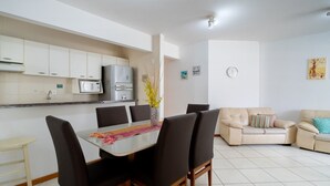A modern kitchen with white cabinets, a microwave, and a refrigerator. There is a dining table with chairs and a sofa in the living area. - 3BR apt W/bbq 240m sea Bombas/sc Cay0123 (Bombinhas)