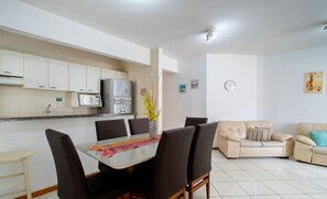 A modern kitchen with white cabinets, a microwave, and a refrigerator. There is a dining table with chairs and a sofa in the living area. - 3BR apt W/bbq 240m sea Bombas/sc Cay0123 (Bombinhas)