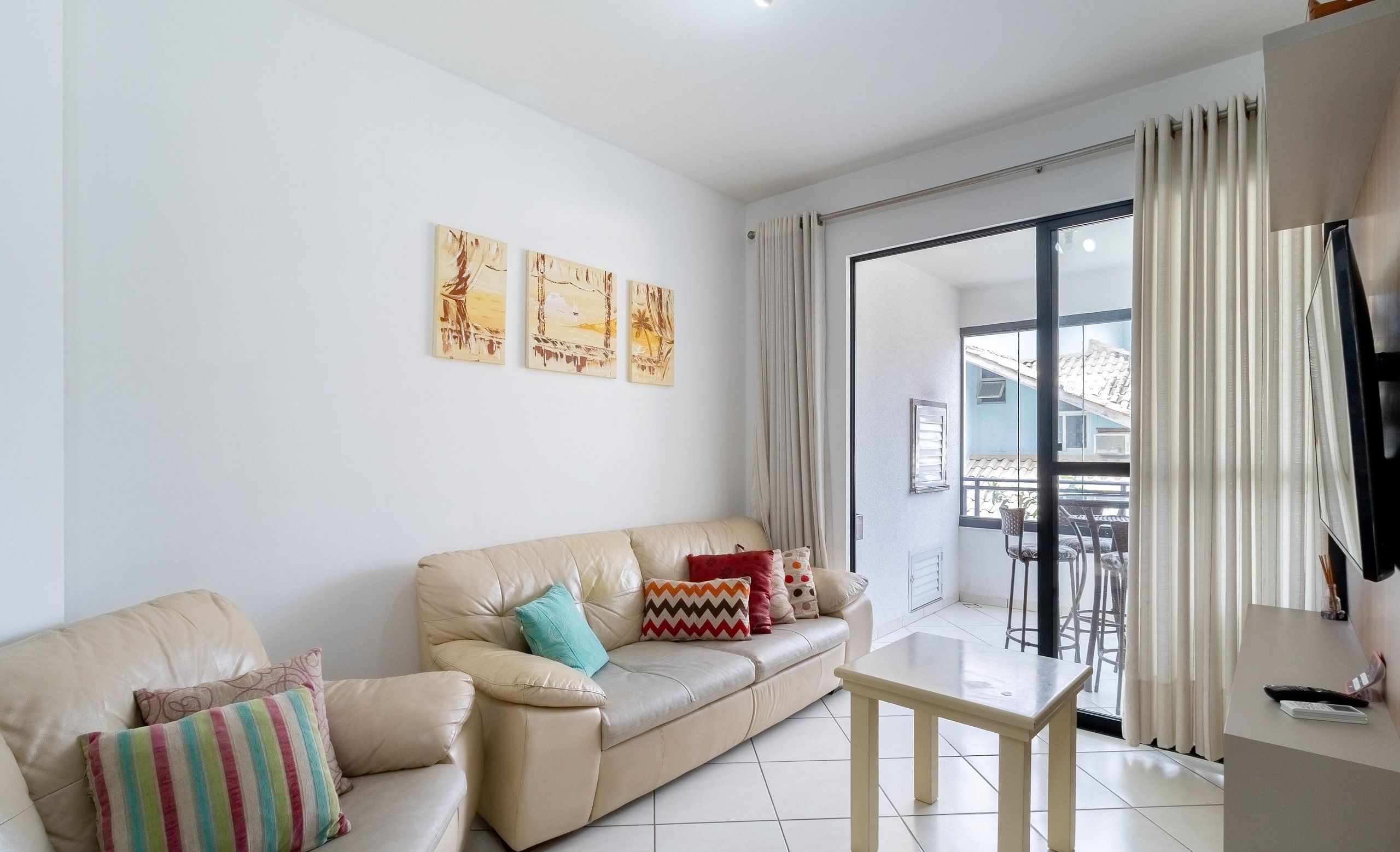 A living room with a beige leather sofa, a small wooden table, and a balcony with a view.