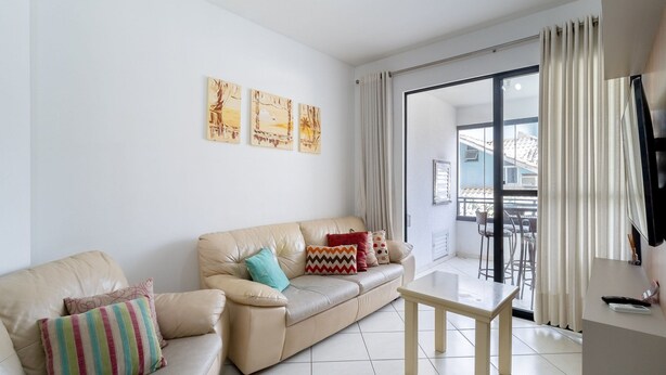 A living room with a beige leather sofa, a small wooden table, and a balcony with a view. - 3BR apt W/bbq 240m sea Bombas/sc Cay0123 (Bombinhas)