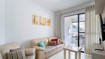 A living room with a beige leather sofa, a small wooden table, and a balcony with a view.