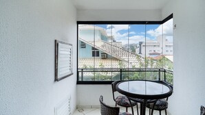 A balcony with a glass door, a round table with chairs, and a framed picture on the wall. - 3BR apt W/bbq 240m sea Bombas/sc Cay0123 (Bombinhas)