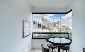 A balcony with a glass door, a round table with chairs, and a framed picture on the wall. - 3BR apt W/bbq 240m sea Bombas/sc Cay0123 (Bombinhas)