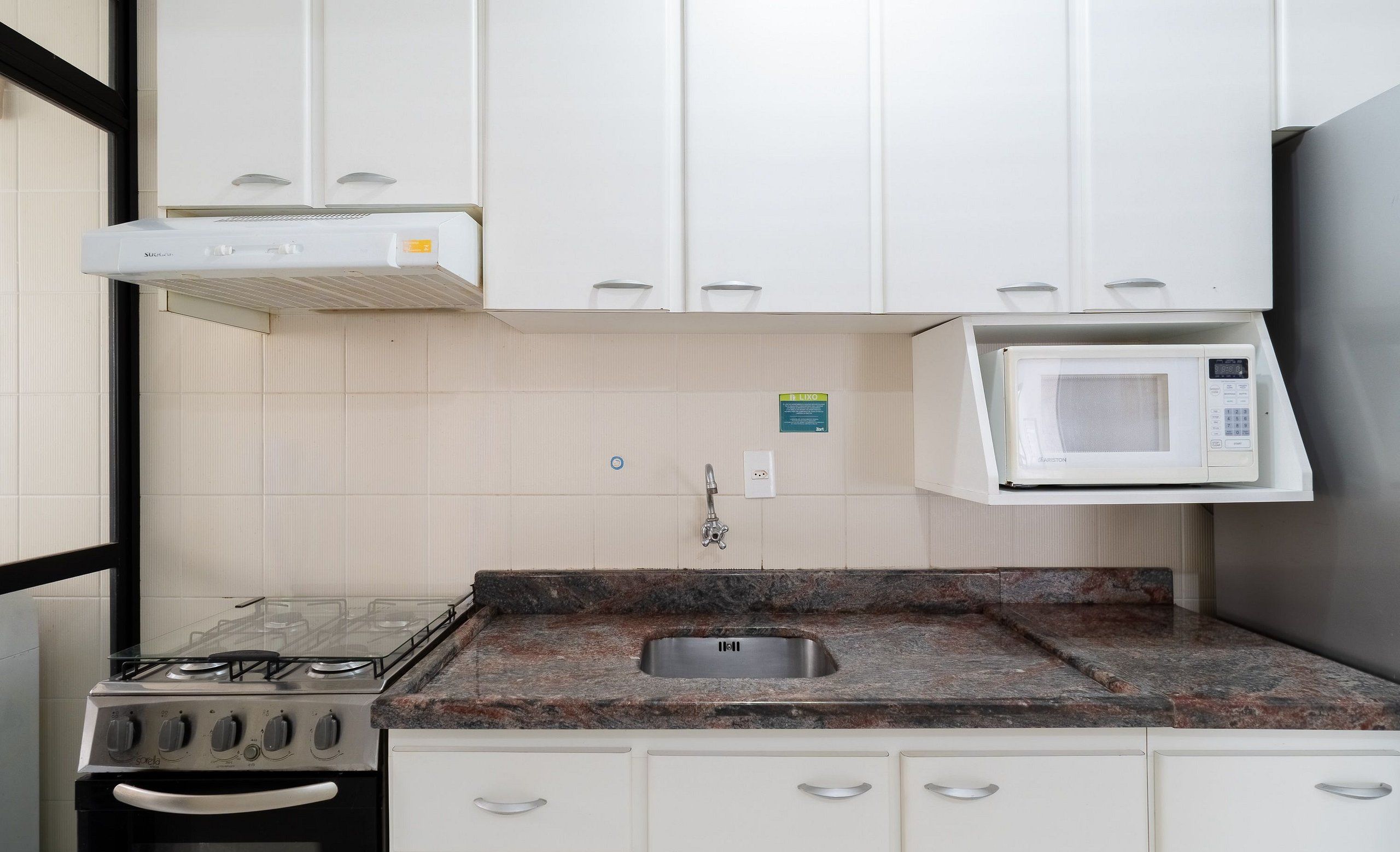A kitchen with white cabinets, a gas stove, a microwave, and a stainless steel sink.
