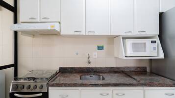 A kitchen with white cabinets, a gas stove, a microwave, and a stainless steel sink.