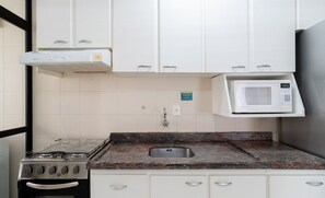 A kitchen with white cabinets, a gas stove, a microwave, and a stainless steel sink. - 3BR apt W/bbq 240m sea Bombas/sc Cay0123 (Bombinhas)