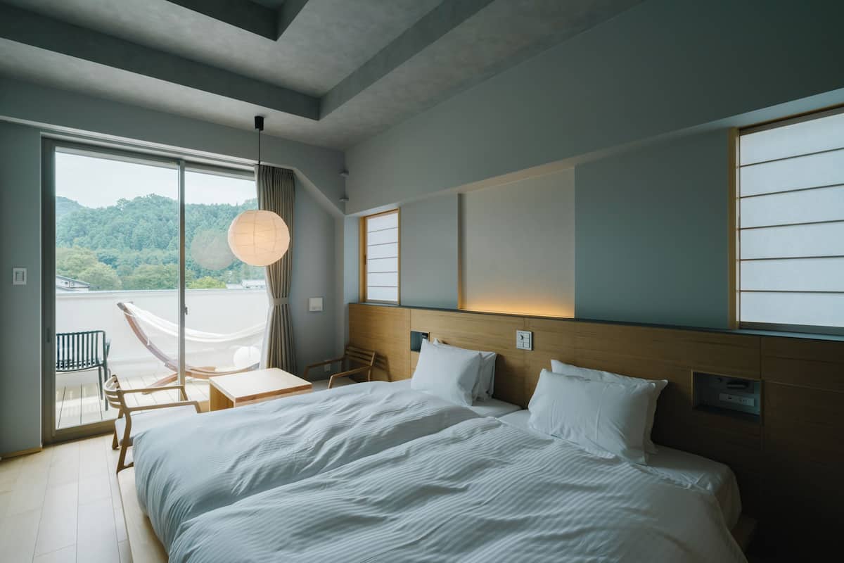 A modern hotel room with a large bed, a balcony with a chair, and a view of the forest.