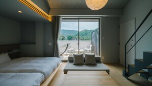 A modern bedroom with a large bed, a sofa with cushions, a staircase, and a view of a balcony with outdoor furniture. - BRANCHERA ISHIBUTAI TERRACE (Asuka)