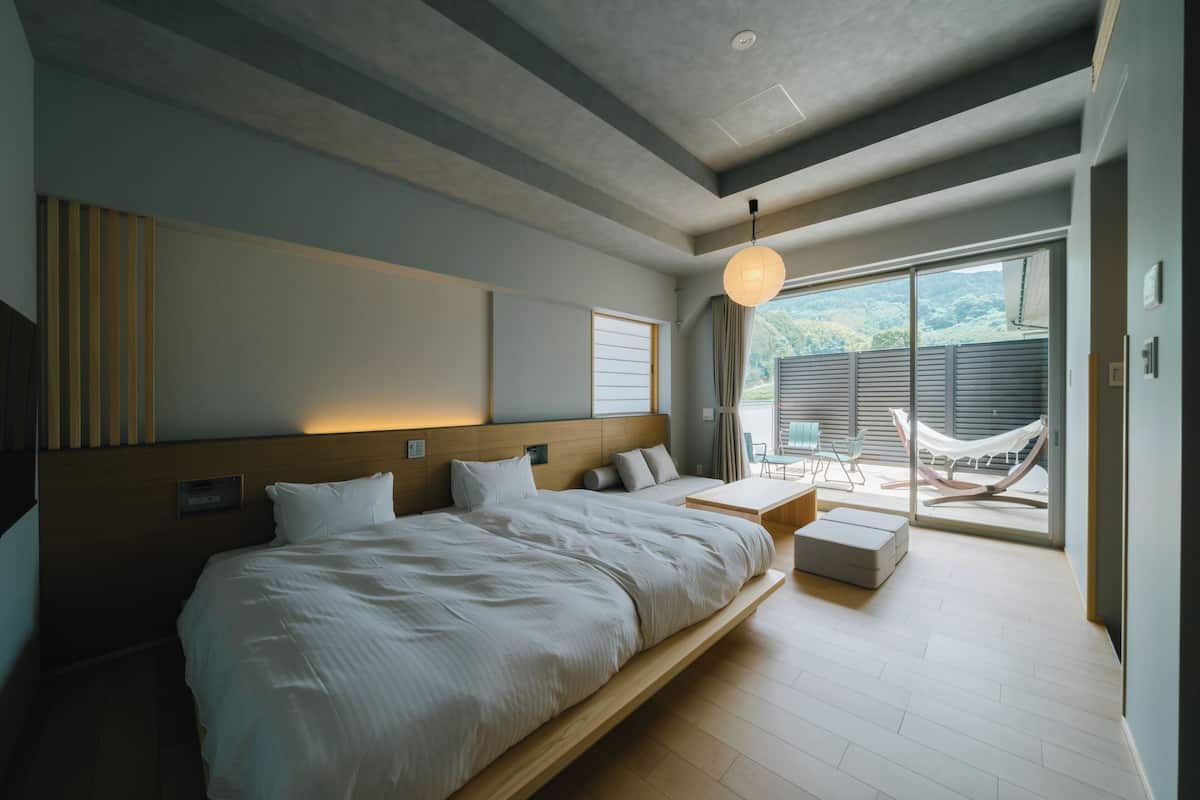 A modern hotel room with a large bed, a small table, and a hammock by the sliding glass door.