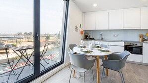 Una cucina moderna con mobili bianchi, un tavolo da pranzo per quattro persone e un'ampia finestra con vista sull'acqua.
