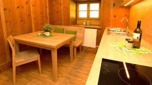 A cozy kitchen with wooden walls, a dining table with chairs, a bench, a window, and a sink with a bottle of wine. - Apartment Typ A by Interhome (Längenfeld)