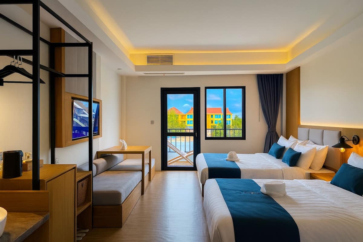 Habitación de hotel con dos camas, un escritorio, una silla y un balcón con vista a edificios.