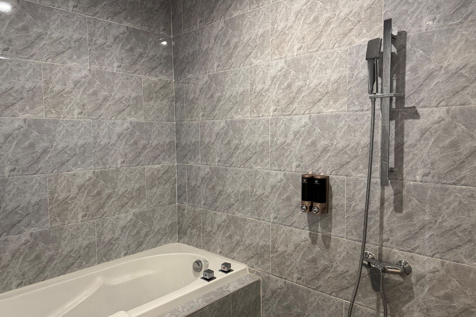 A bathroom with a bathtub, a shower, and a wall-mounted hand dryer.