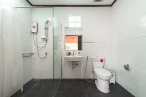 Une salle de bain avec une douche à parois de verre, un lavabo blanc, des toilettes et une petite fenêtre au-dessus du miroir.