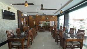 Un espace repas doté de plusieurs tables et chaises en bois, de ventilateurs de plafond et de luminaires suspendus.