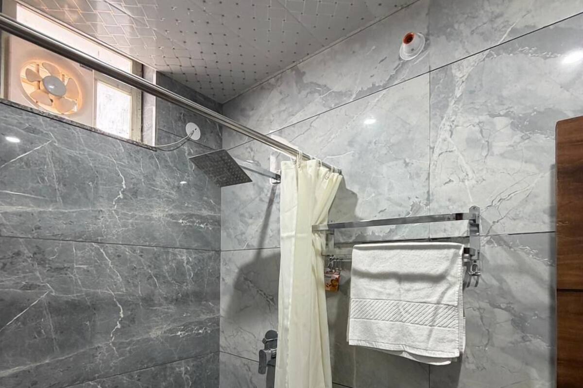 Une douche avec un rideau blanc, un porte-serviettes avec une serviette, et un plafond à motifs géométriques.