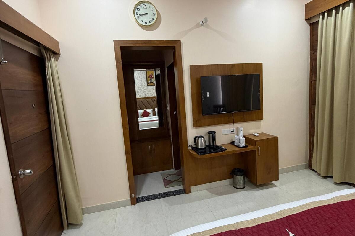 Une chambre d’hôtel avec un lit, une télévision, un bureau en bois, une horloge et une porte.