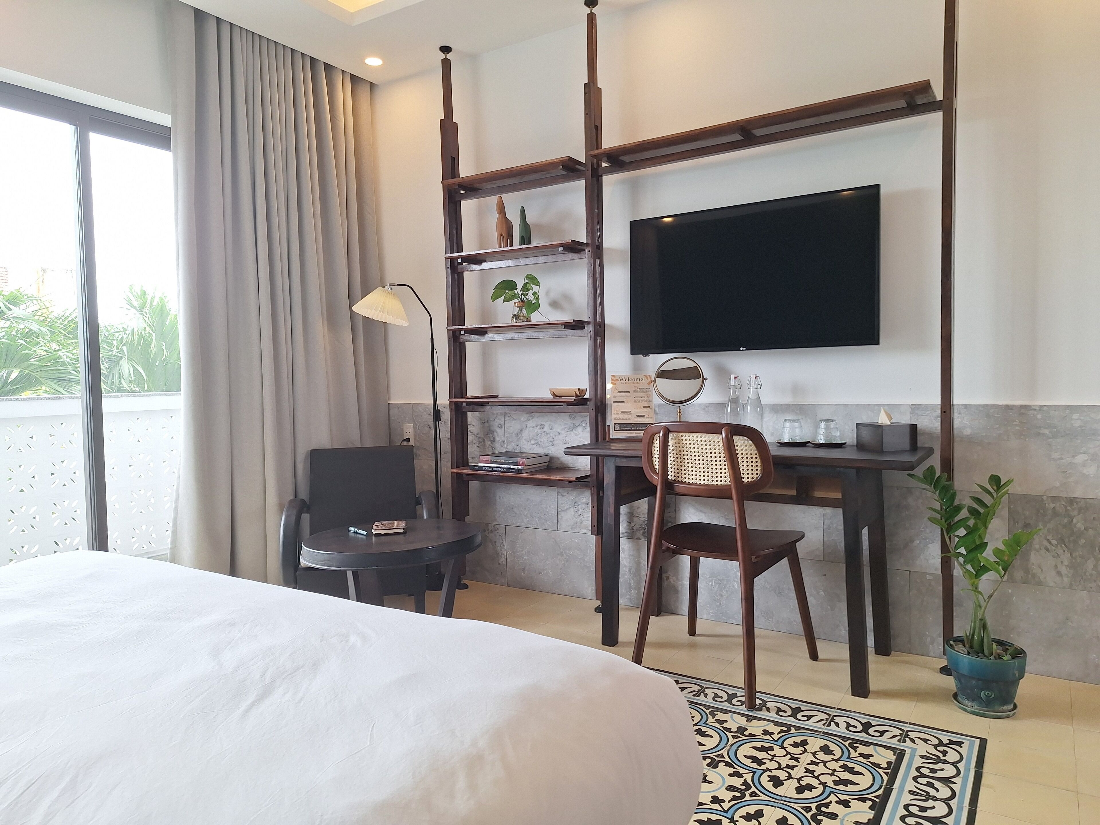 A hotel room with a bed, a desk with a chair, a television, and a potted plant.