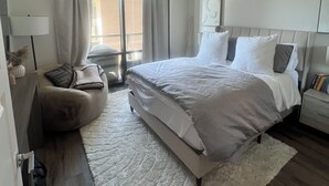 A modern bedroom with a large bed, a ceiling fan, a window with curtains, a small bedside table with books, and a fluffy rug. - Ultra Chic 1-bedroom apartment with AC, fitness room in cool Austin (Austin)