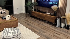 A modern living room with a flat-screen TV mounted on a wooden wall, a wooden coffee table, a striped ottoman, and a potted plant. - Ultra Chic 1-bedroom apartment with AC, fitness room in cool Austin (Austin)